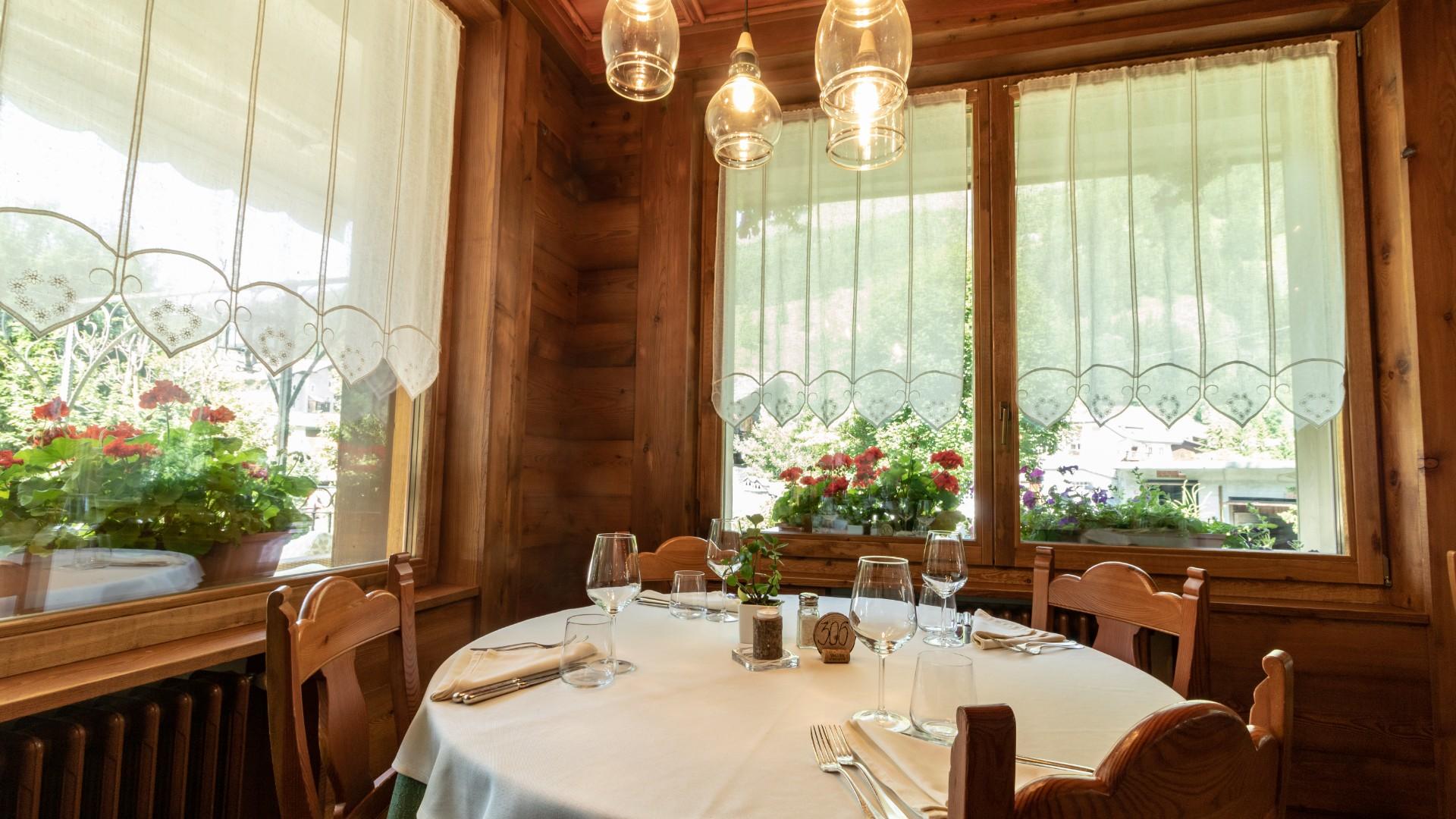 Cozy restaurant with a set table, curtains, and flowers by the window.